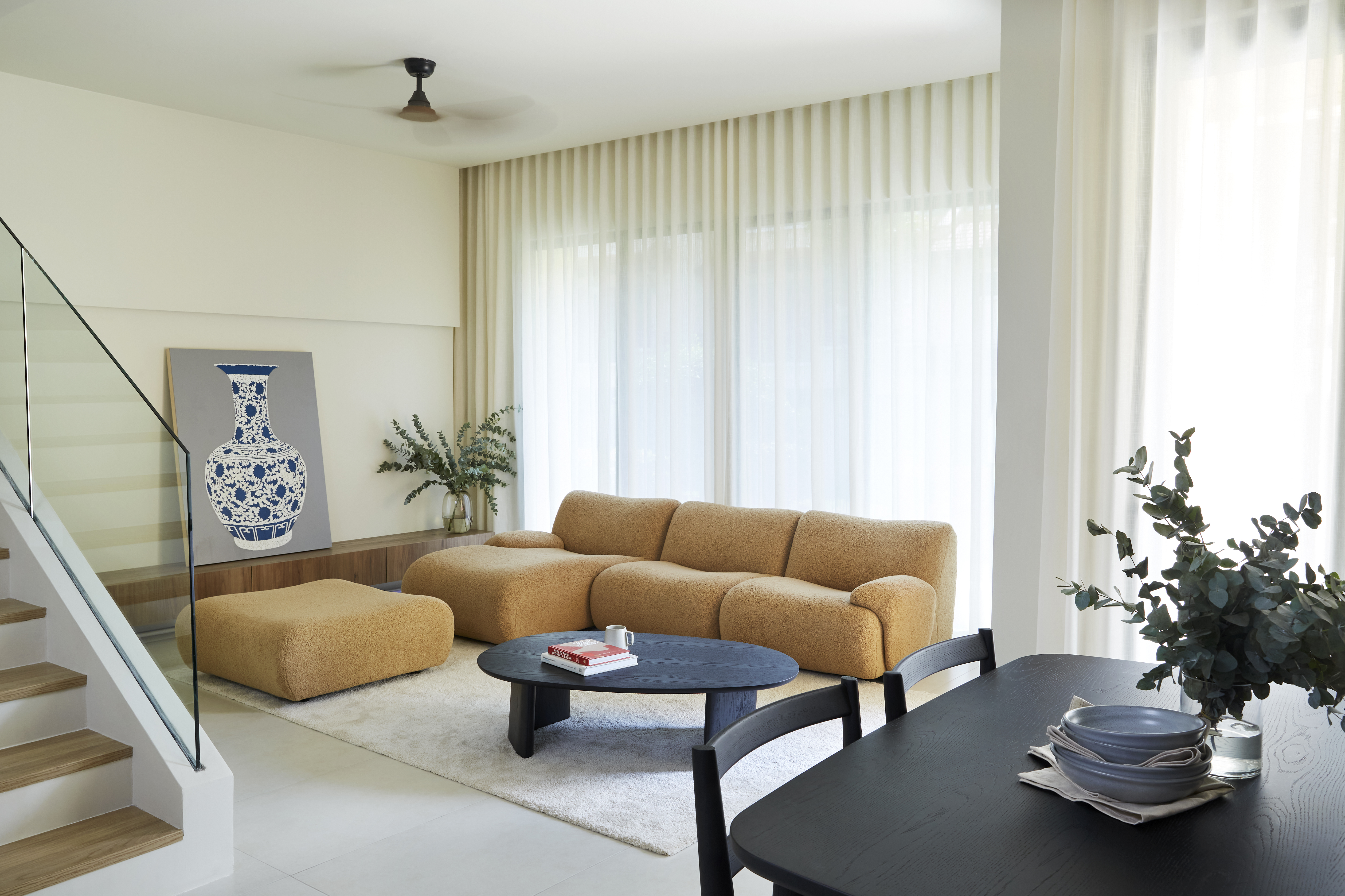 Bright living room with a tan modular sofa, black coffee table, and dining table in the foreground.